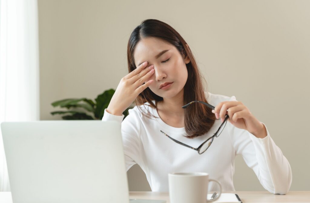 Woman rubbing her eyes while holding glasses, possibly experiencing dry eyes from computer use.