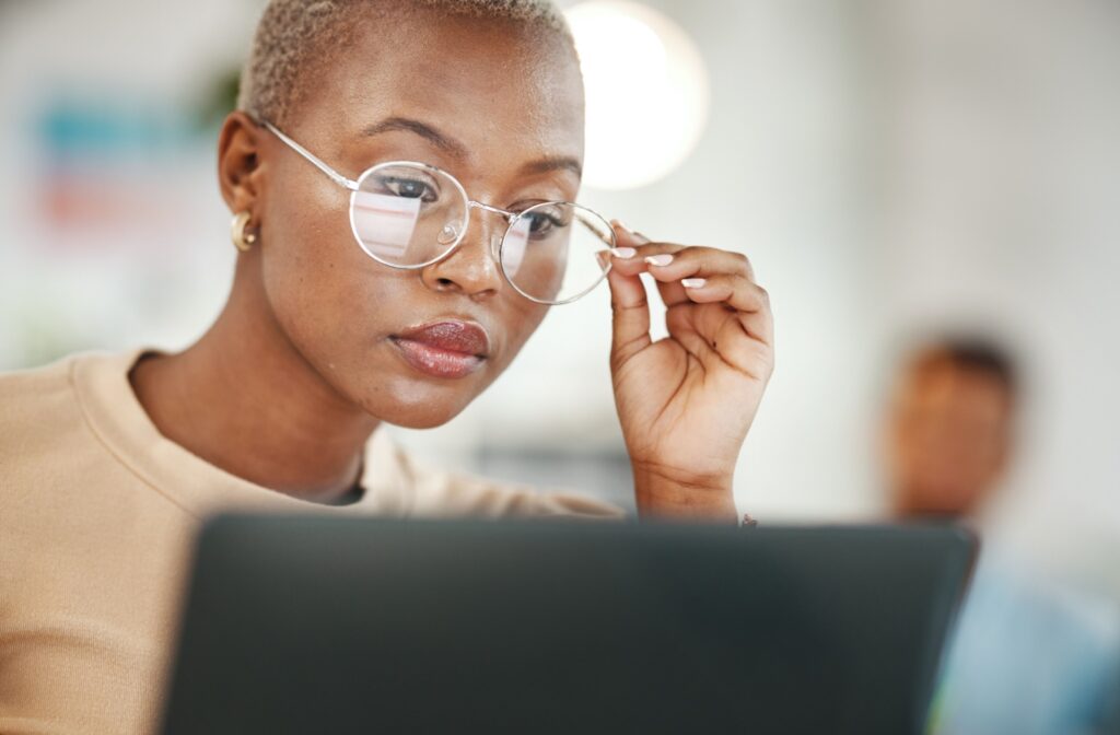 Woman adjusting her glasses while working on a computer, focusing on screen.