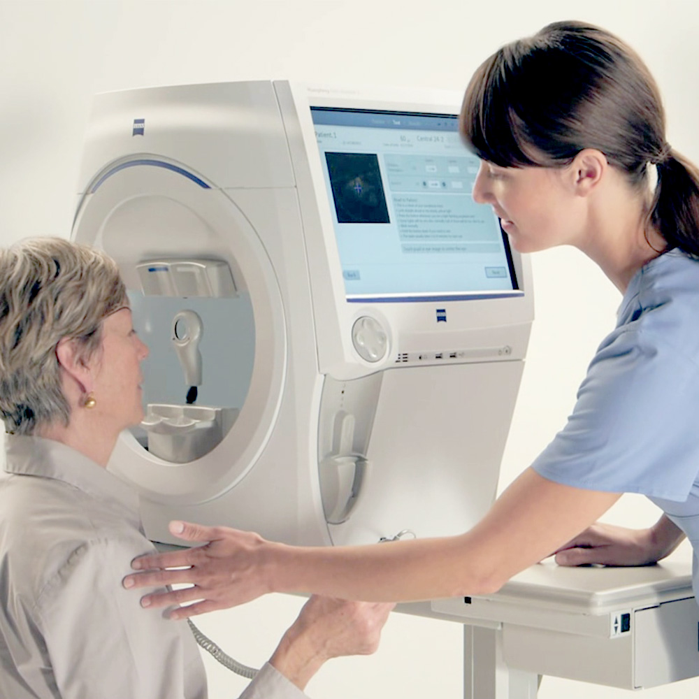 An eye care professional assists a patient using a visual field testing machine during an eye exam.